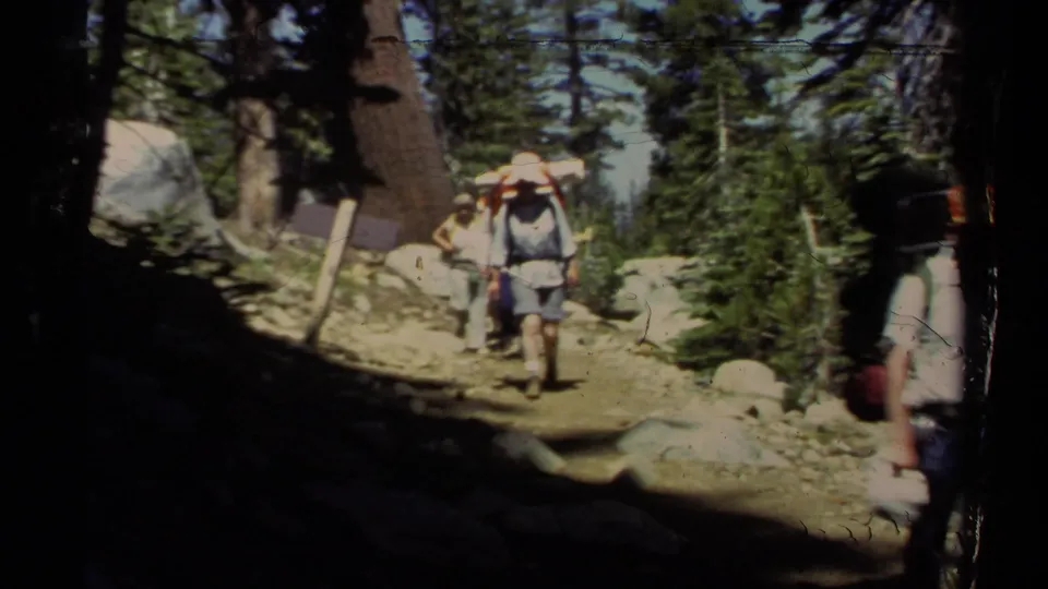 Lake Tahoe 1978 home-movie frame showing backpackers in hats walking through alternating shade and sunlight.