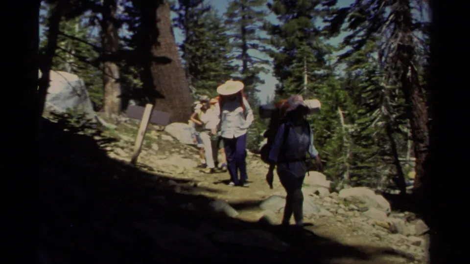 1978 Lake Tahoe 8mm frame with a dark-jacketed hiker in the foreground and backpackers behind on a forest path.