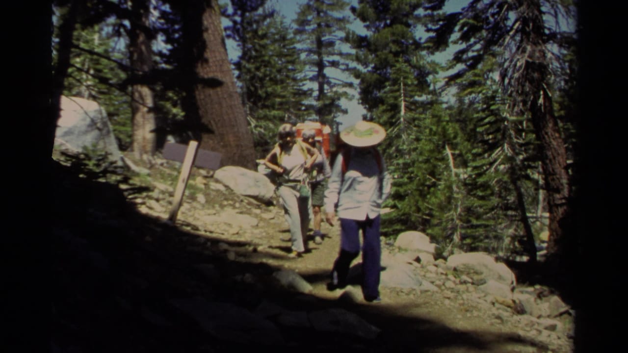 1978 Lake Tahoe 8mm frame of hikers with packs and hats approaching through a rocky conifer trail.