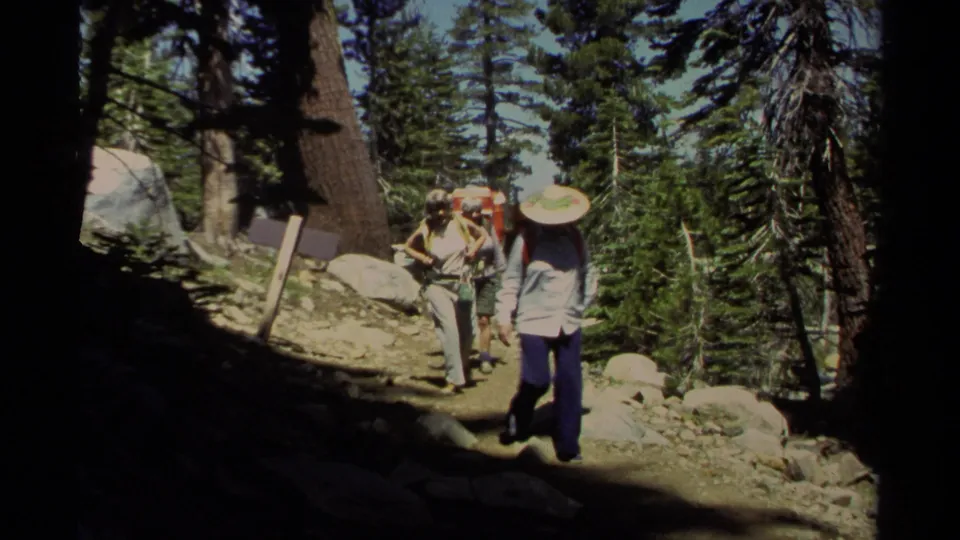 1978 Lake Tahoe 8mm frame of hikers with packs and hats approaching through a rocky conifer trail.