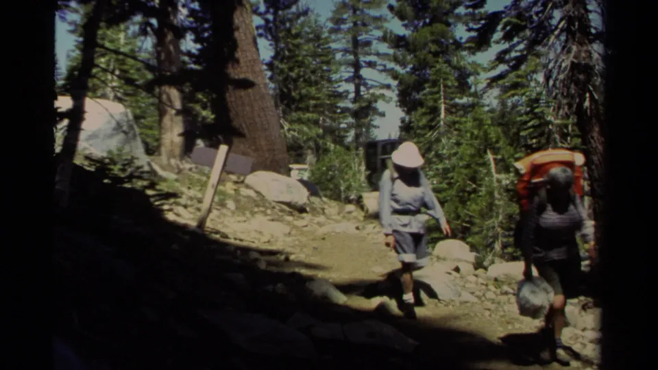 1978 Lake Tahoe home-movie frame of backpackers walking through dappled light on a rugged pine forest path.