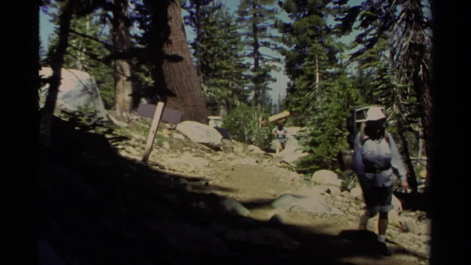1978 Lake Tahoe frame showing a backpacker approaching the camera on a rocky trail among pines and boulders.
