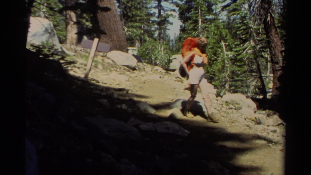 Woman with orange backpack walking on a rocky forest trail.