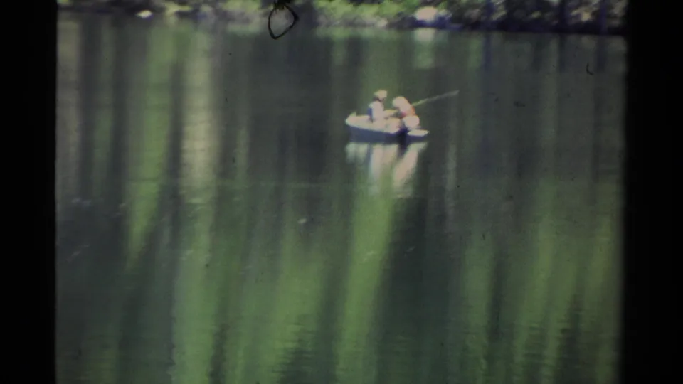 1978 Lake Tahoe 8mm frame showing two people in a small boat on calm water with soft pine reflections and visible film grain.