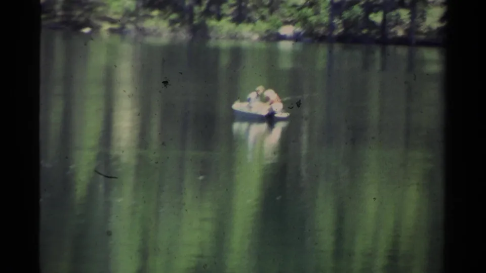 Soft 8mm Lake Tahoe frame from 1978 showing a small boat with two distant people on still water, with pine reflections and minor film marks.