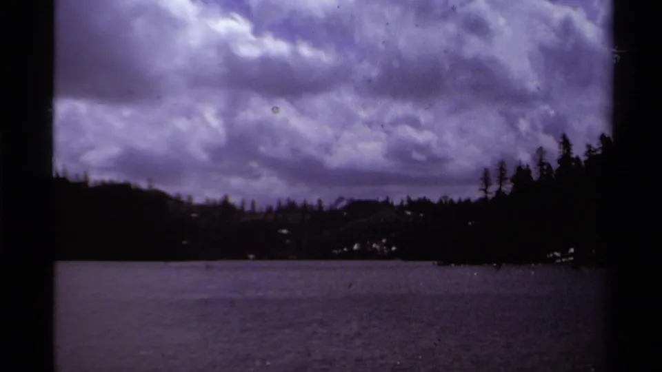 Lake Tahoe shoreline appears under layered clouds, with dark pines framing the 1978 8mm home-movie view.