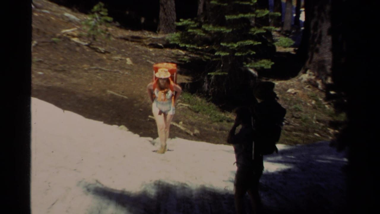 In 1978 Lake Tahoe footage, a woman in a straw hat and orange backpack approaches across patchy snow as a second hiker waits in shade.