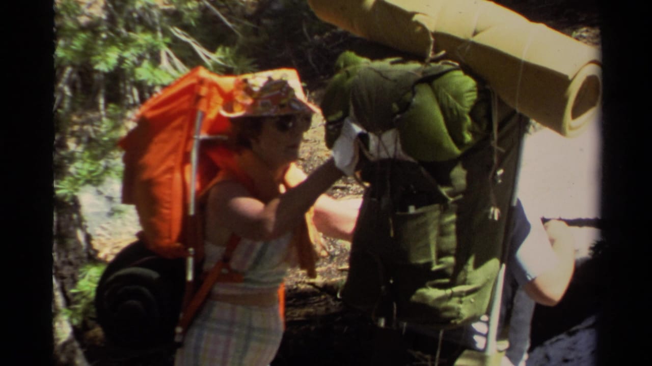 Close view of a hiker adjusting a green backpack while wearing an orange pack and sun hat.