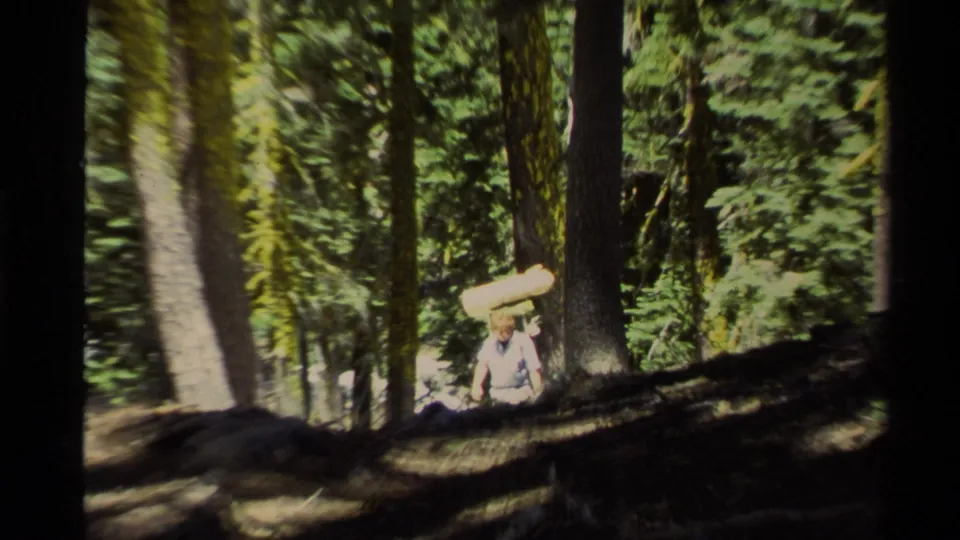 The adult hiker is more centered on the Lake Tahoe forest slope, walking uphill with a rolled sleeping mat or pad.