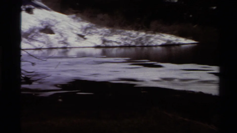 Lake Tahoe 8mm frame from 1978 with rippled dark water, snow on the far bank, and shaded trees above the shoreline.