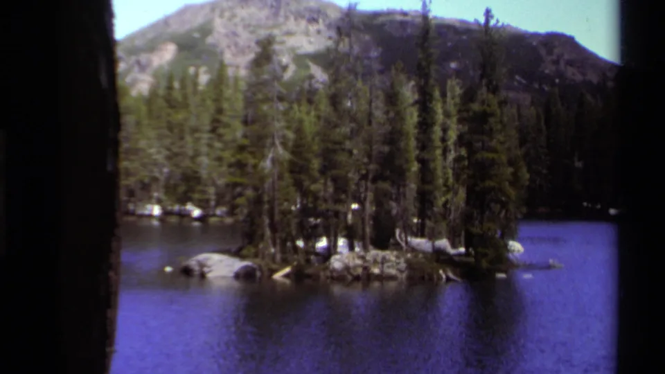 1978 Lake Tahoe home-movie frame shows a wooded island in blue water with a mountain rising beyond the trees.