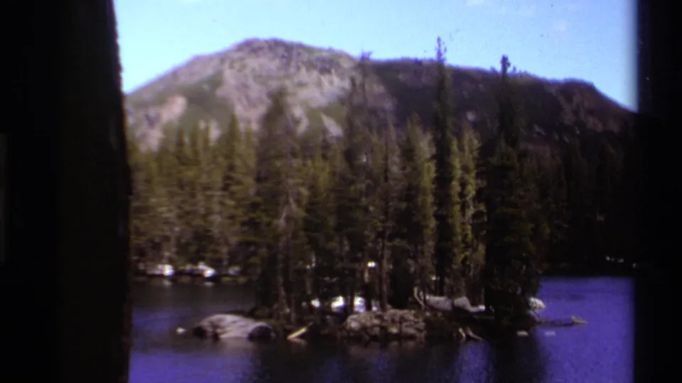 Lake Tahoe 8mm frame with a small evergreen island, dark blue lake water, and a rocky mountain under clear sky.