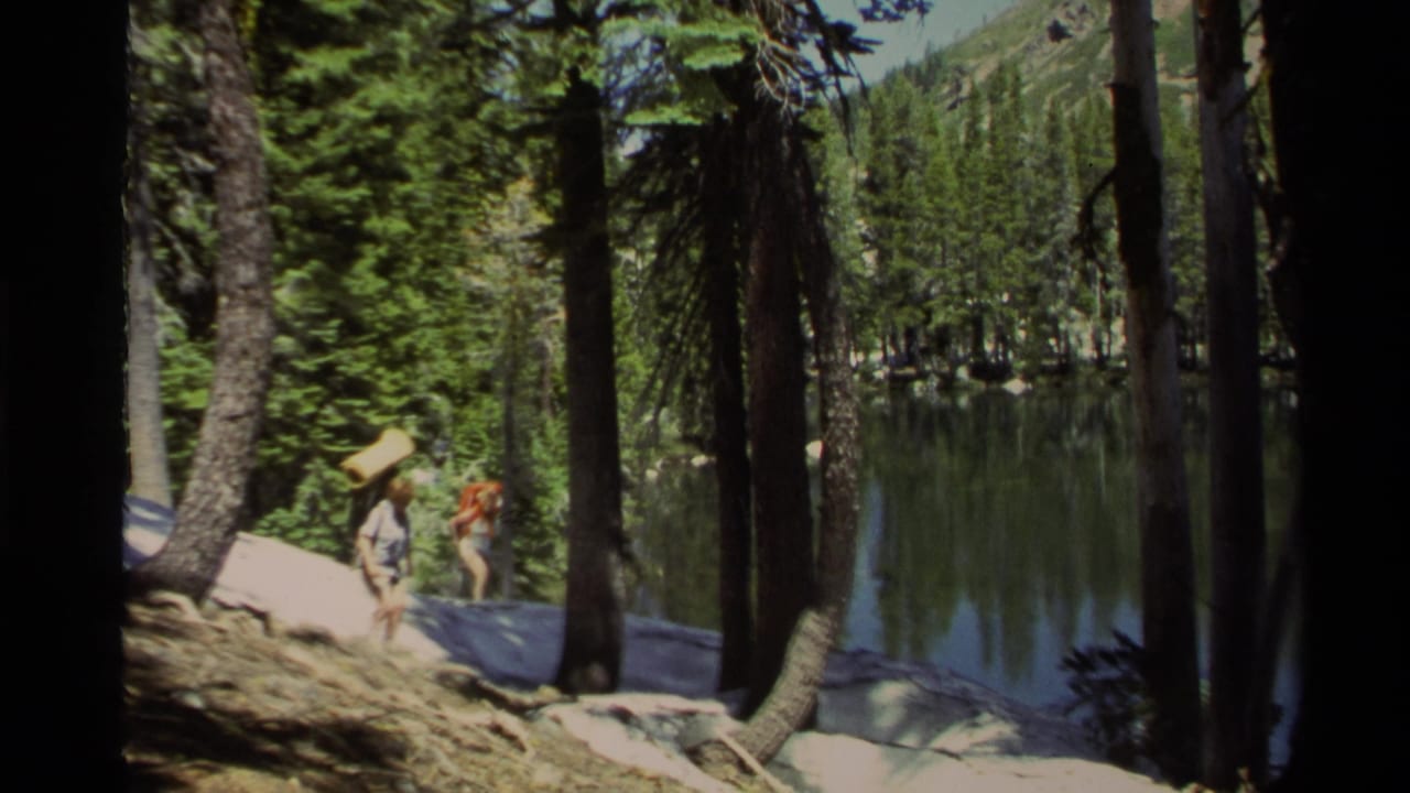 In Lake Tahoe home-movie footage from 1978, two backpacked hikers move through pine trees near a reflective lakeshore.