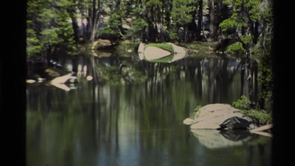 The 1978 Lake Tahoe clip lingers on a reflective forest lake bordered by evergreens and pale shoreline rocks.