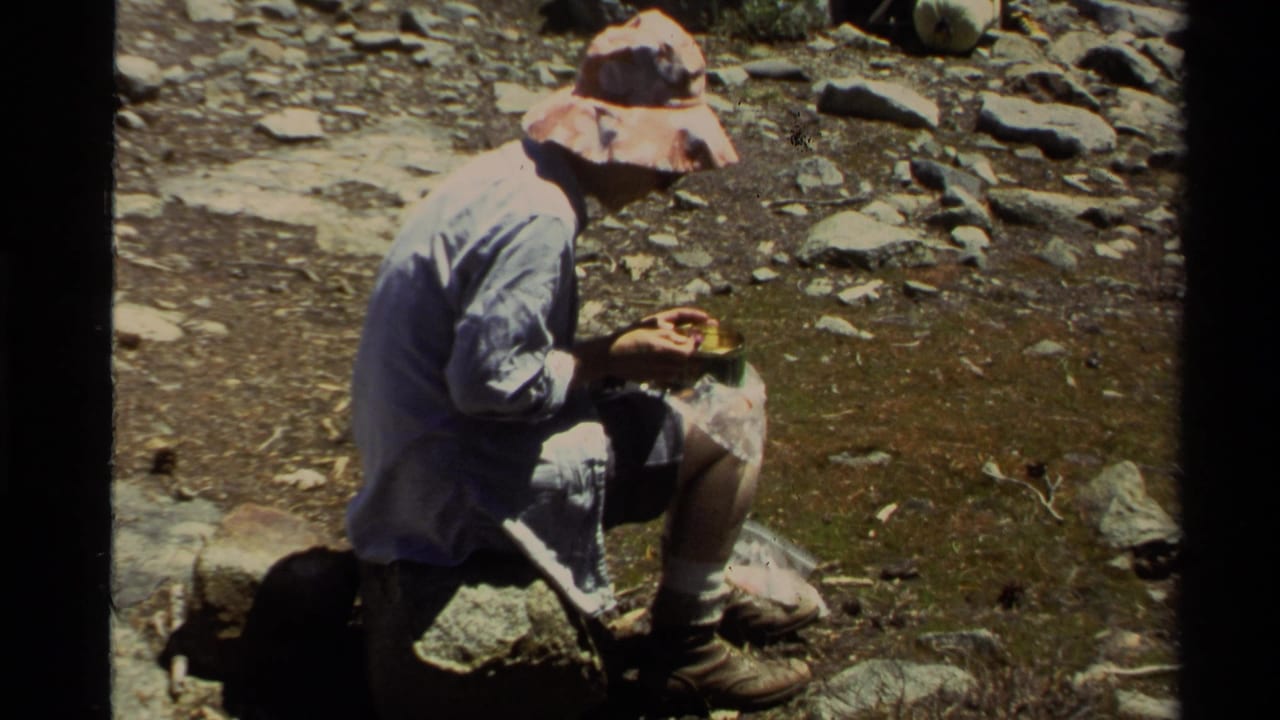 1978 Lake Tahoe 8mm frame of a hiker in a wide-brimmed hat sitting on a rock and eating during a trail break.