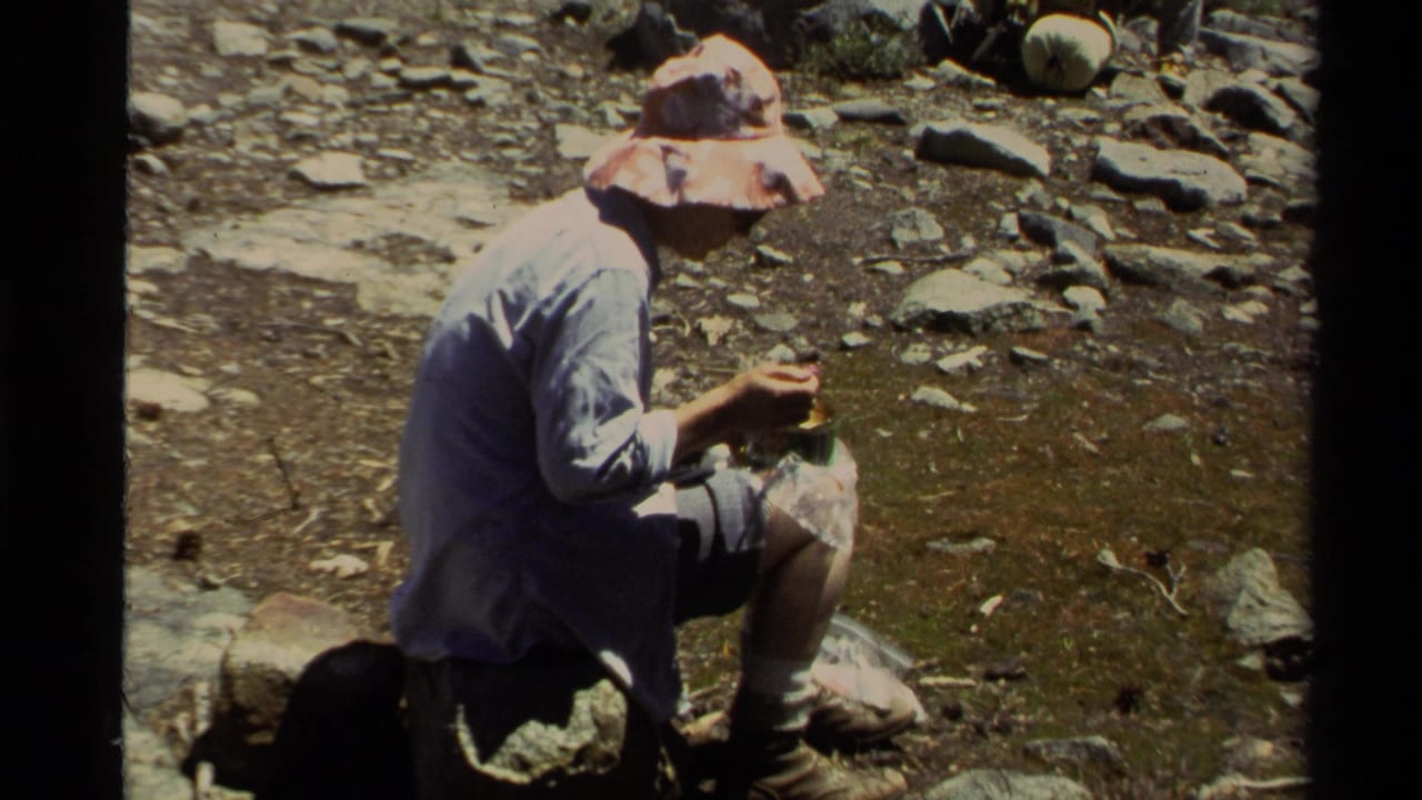 1978 Lake Tahoe home-movie frame showing a seated hiker eating from a small container on rocky ground.