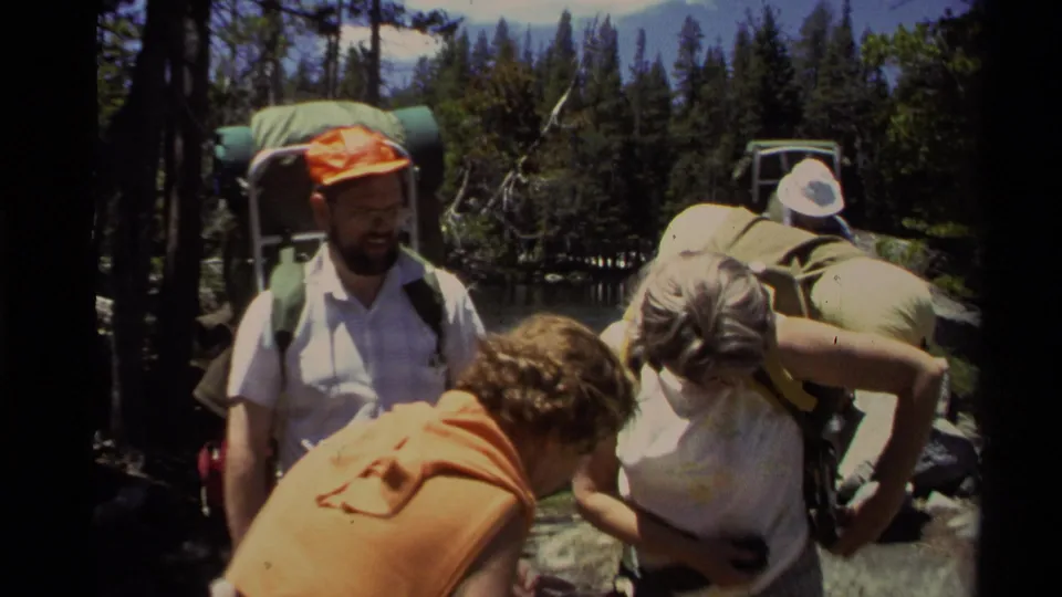 1978 Lake Tahoe frame of backpackers near a lake, with one person adjusting gear and others standing nearby.