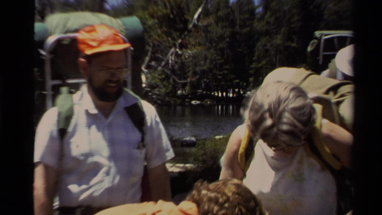 1978 Lake Tahoe home-movie frame showing adult hikers with backpacks beside trees and lake water.