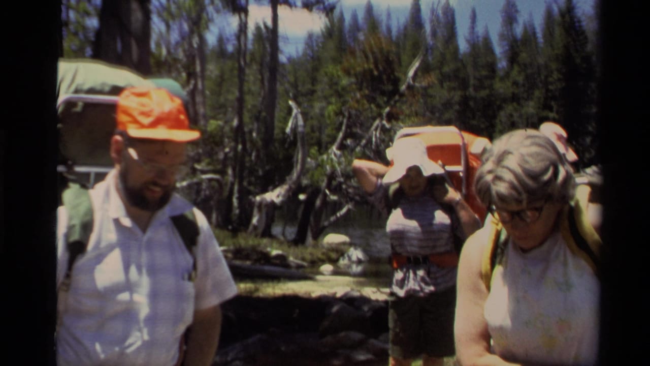 1978 Lake Tahoe home-movie frame showing adults with backpacks on a forest trail near a lake or stream.