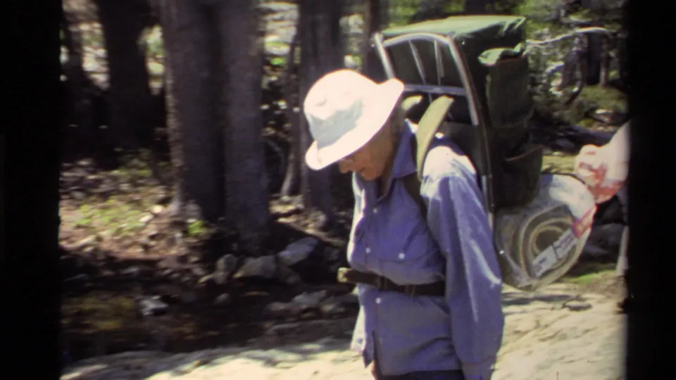 1978 Lake Tahoe frame of an adult backpacker with an external-frame pack walking along a wooded path.
