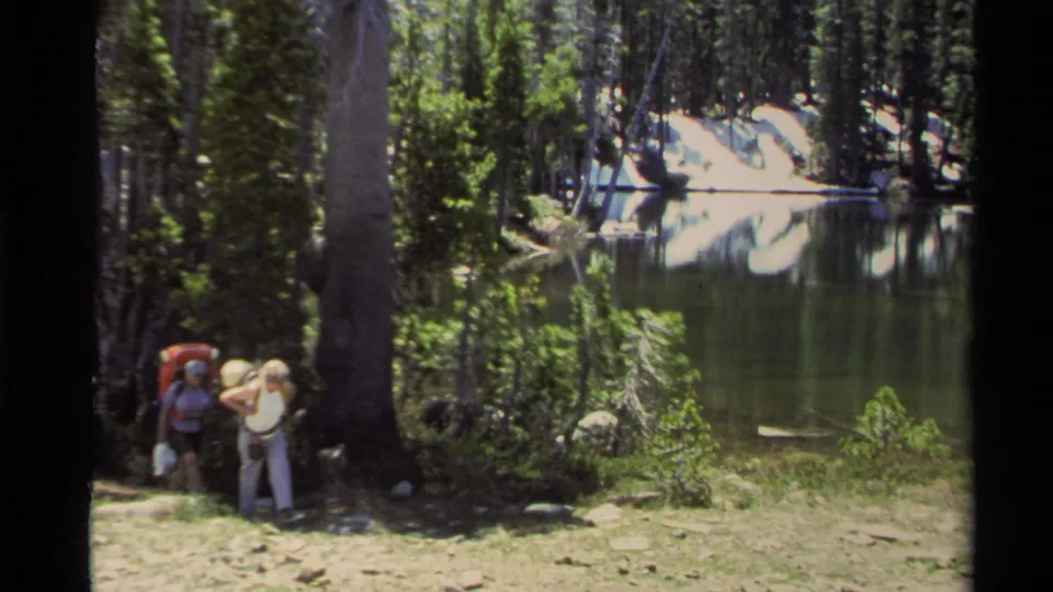Lake Tahoe forest scene with two backpackers near a calm lake, filmed as 1978 home-movie footage.
