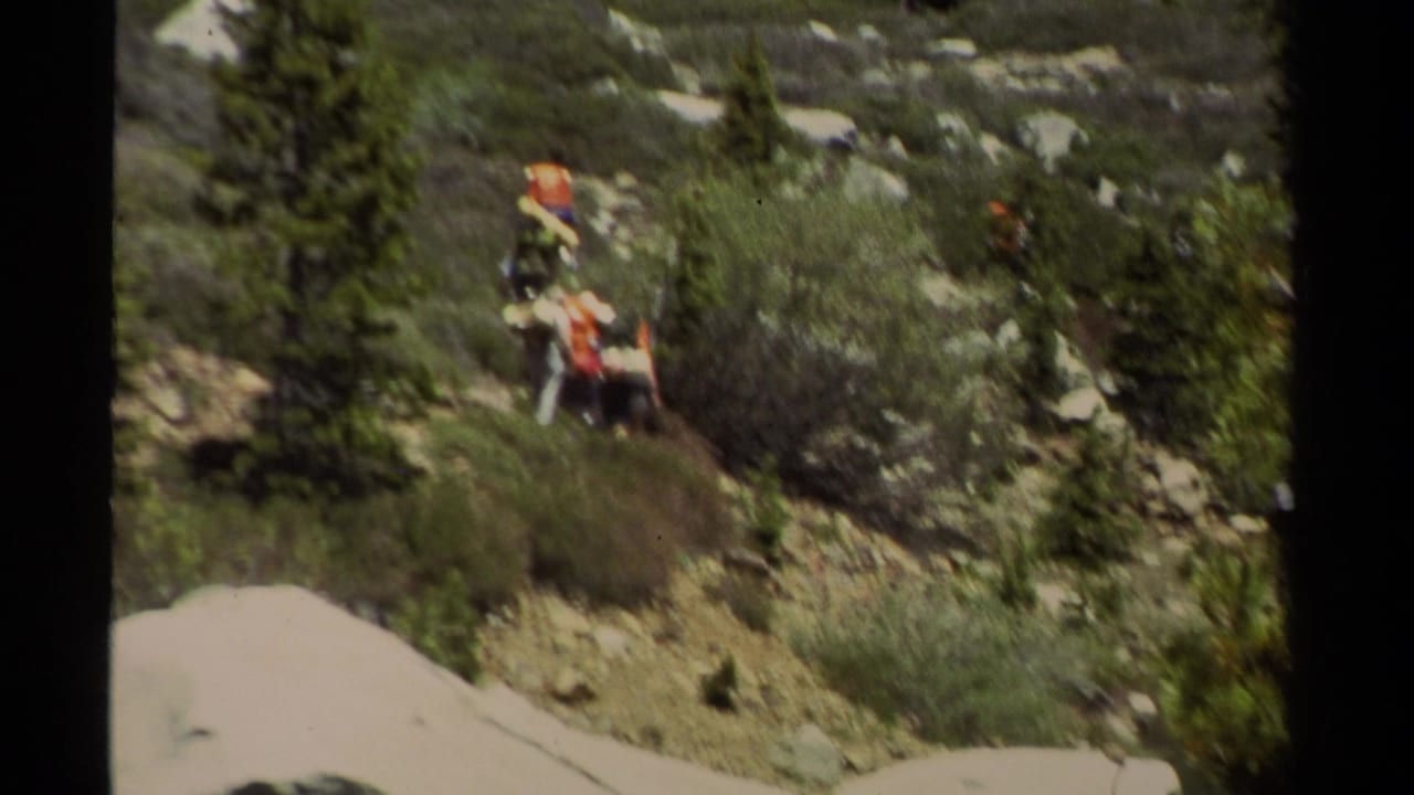 1978 Lake Tahoe home-movie frame showing hikers in orange and red clothing on a rocky slope above an alpine lake.