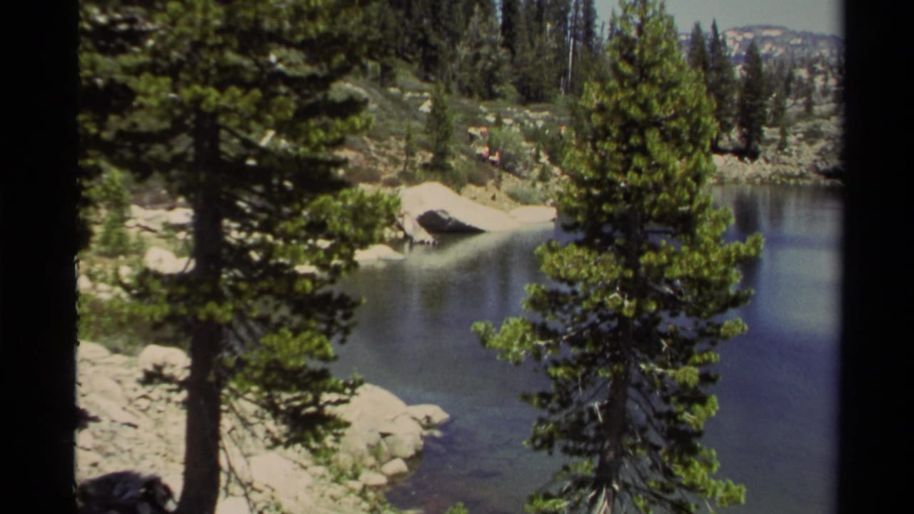Evergreen trees and rocks frame a clear mountain lake.