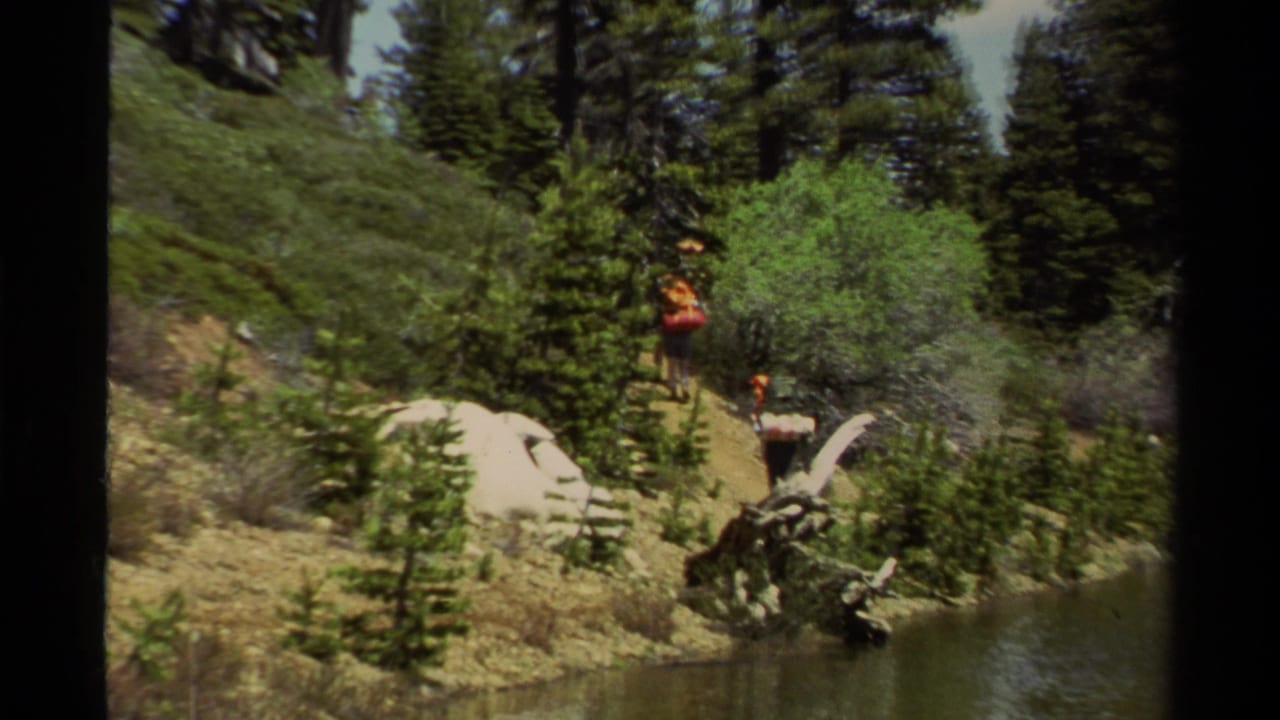 1978 Lake Tahoe hiking scene with backpackers carrying gear along a rocky trail near water and pine forest.