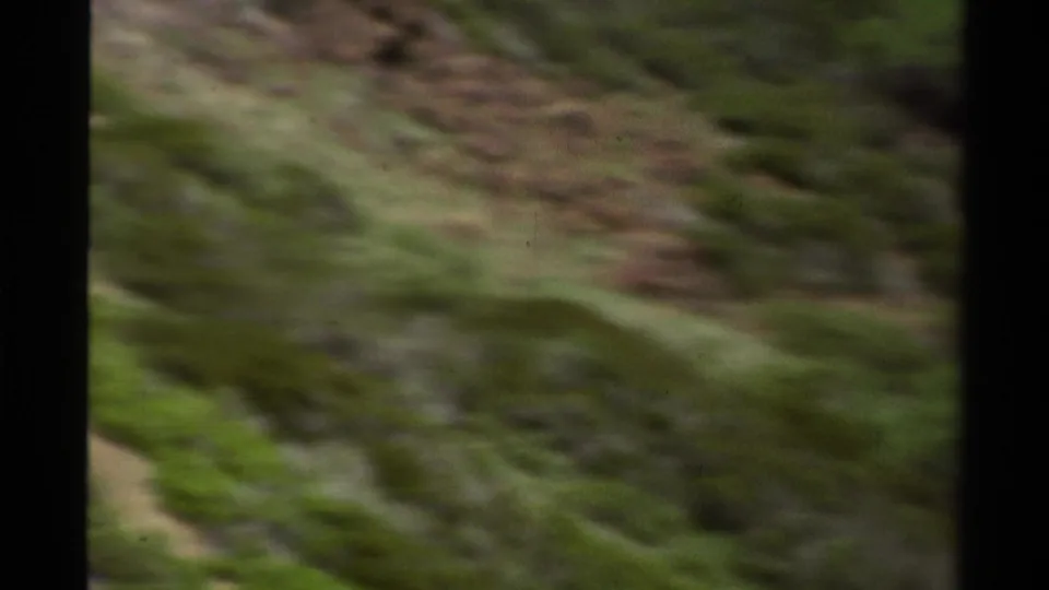 A soft 1978 Lake Tahoe frame shows a grassy, rocky slope during a fast handheld or moving-vehicle camera pass.