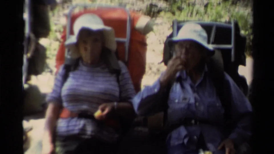Close 1978 Lake Tahoe home-movie frame of two women backpackers resting, with hats, packs, and trail gear visible.