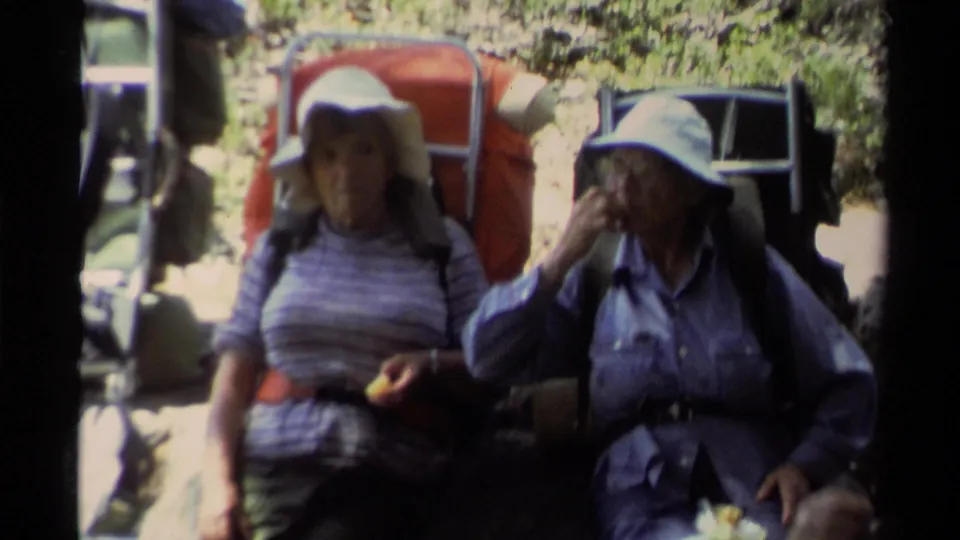 Lake Tahoe 1978 home-movie frame showing two women in sun hats and large backpacks resting on a shaded forest trail.