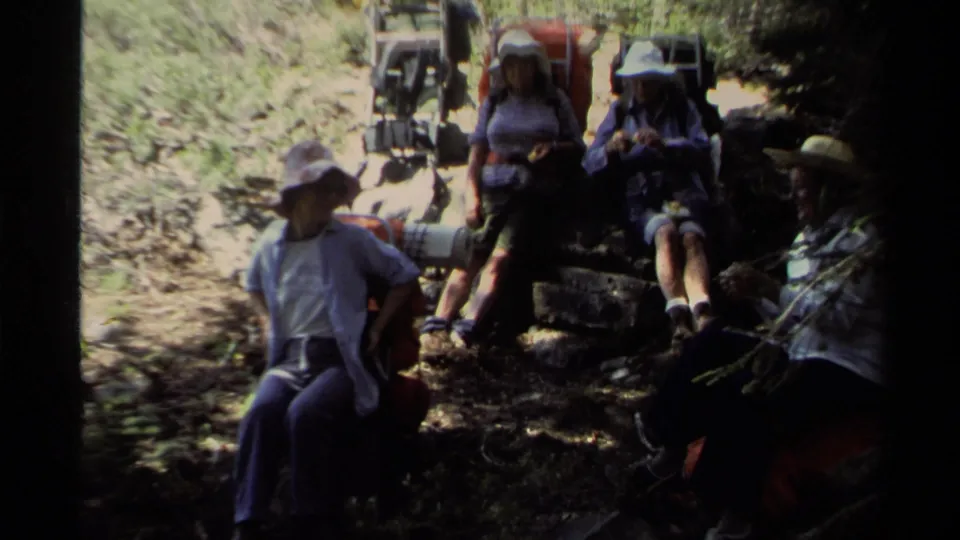 Lake Tahoe 1978 home-movie frame showing a shaded hiking group resting near rocks, packs, and dry forest ground.