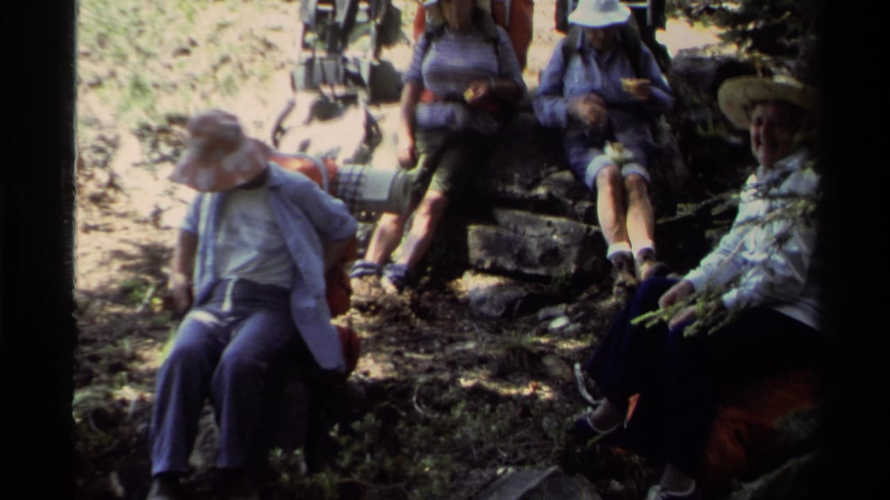 Hikers rest on rocks along a shaded forest trail with packs and hats visible.