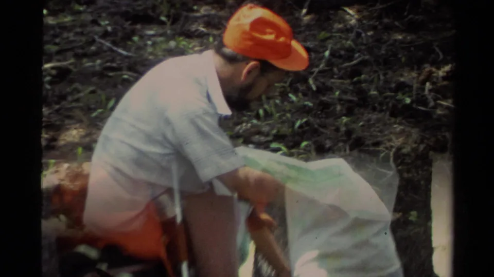 1978 Lake Tahoe home-movie frame with a hiker reading a map while a nearby figure partly crosses the foreground.
