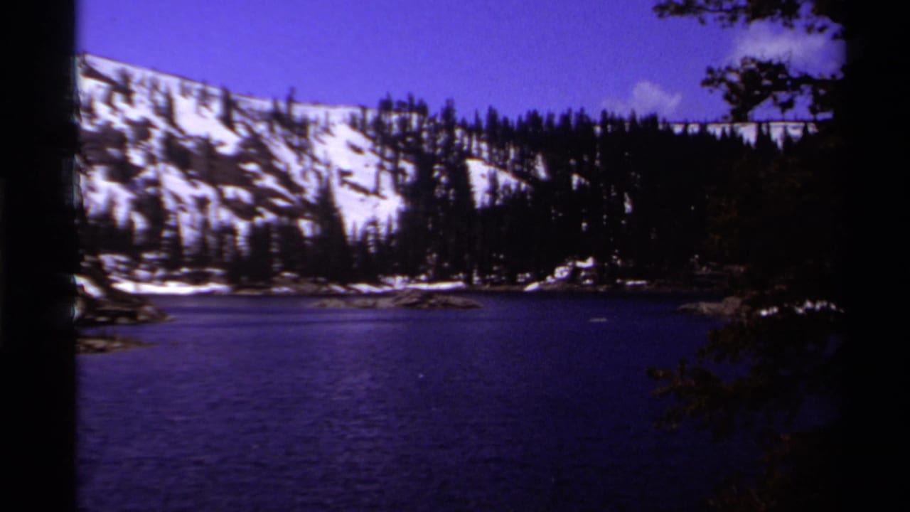 Calm blue lake below snowy mountain slopes and evergreen trees.