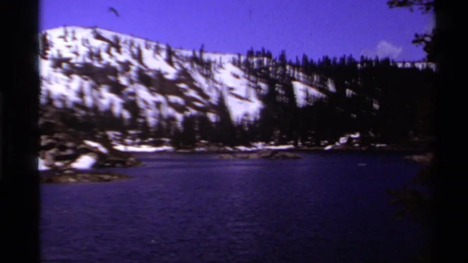 1978 Lake Tahoe frame with a dark blue lake in the foreground, snowy ridge beyond, evergreen trees, and shadowed film edges.