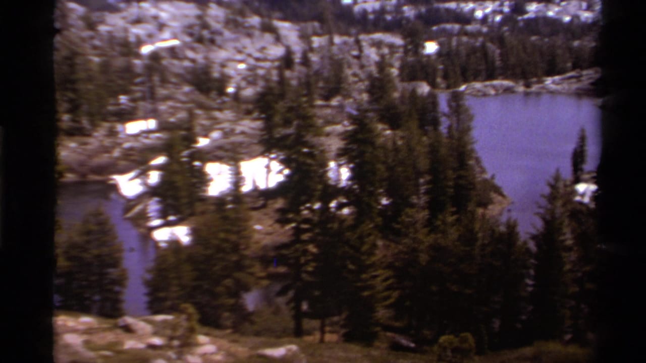 1978 8mm Lake Tahoe-region view of an alpine lake seen from above, framed by evergreens and lingering snow.