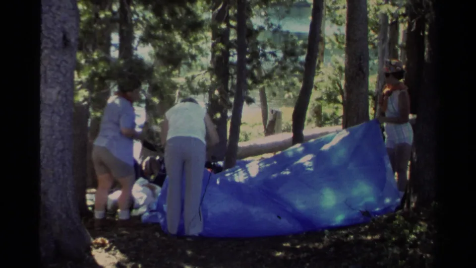 The group clusters beside the blue tarp in a 1978 Lake Tahoe forest campsite scene.