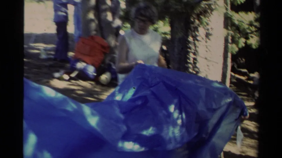 Close home-movie view of a camper behind a blue tarp during setup in a Lake Tahoe forest campsite.
