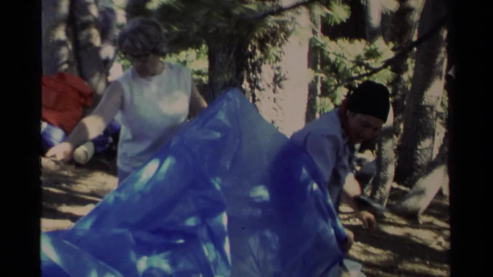 Lake Tahoe camping scene with two adults handling a blue tarp in a wooded area, filmed in 1978 on 8mm.