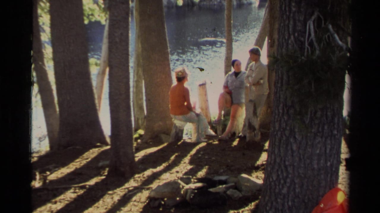 1978 Lake Tahoe frame of adults relaxing and talking beside the water under tall shoreline trees.