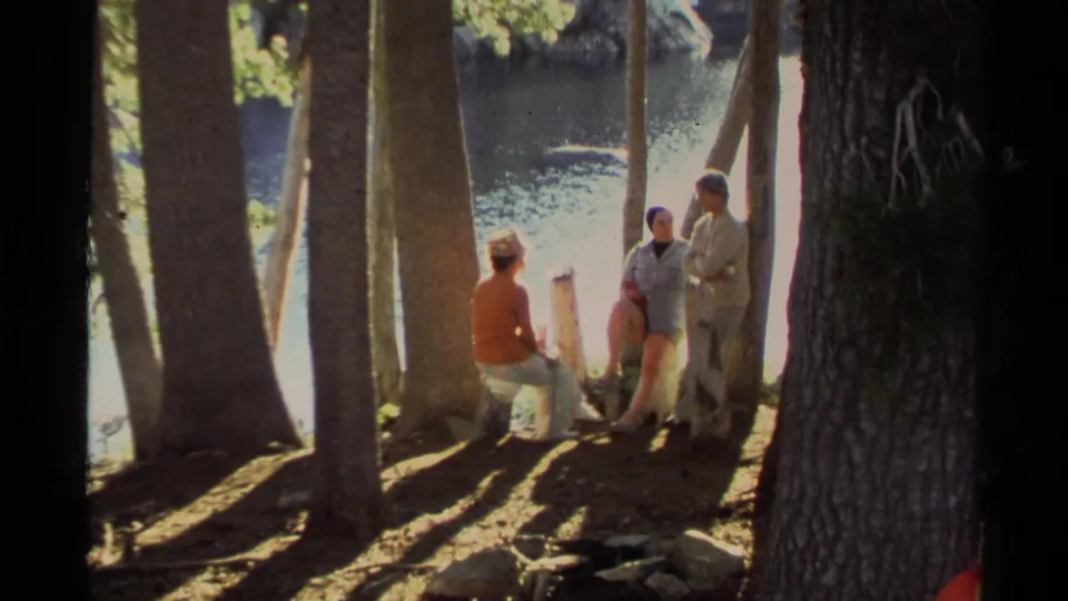 1978 Lake Tahoe home-movie view of campers resting near trees along a bright lakeside bank.