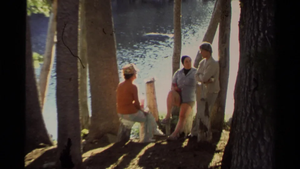 1978 Lake Tahoe frame showing adults in casual clothing resting and talking beside shoreline trees.
