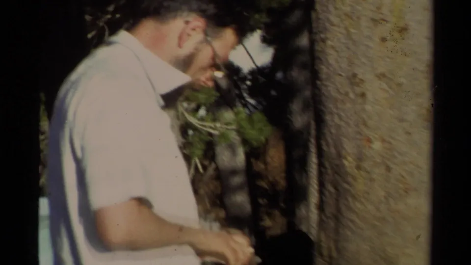 1978 Lake Tahoe frame showing an adult man in a light shirt near a large tree trunk, filmed with soft handheld 8mm focus.
