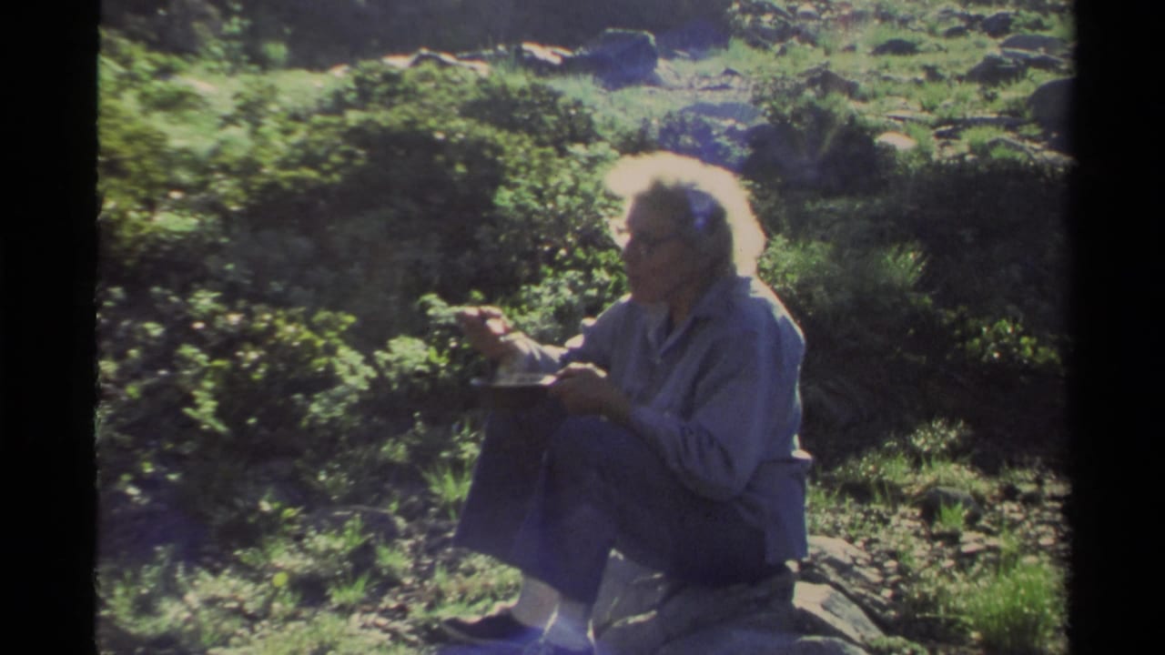 Adult woman with white hair and glasses sits on a rock eating from a plate in 1978 Lake Tahoe home-movie footage.