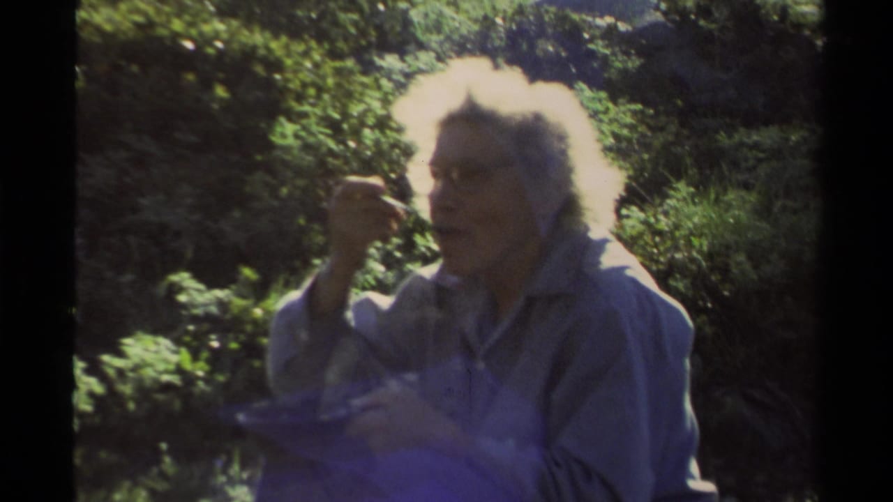 Close view of a white-haired woman eating while seated outdoors.