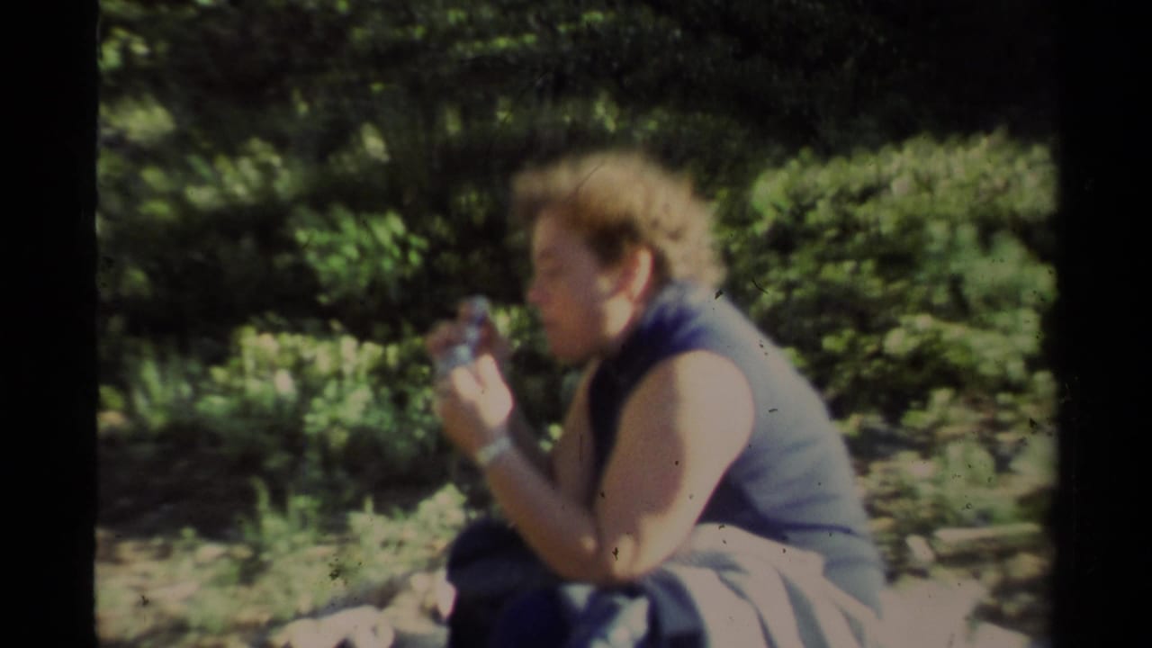 1978 Lake Tahoe home-movie frame showing an adult in a sleeveless top seated outdoors and eating in a wooded area.