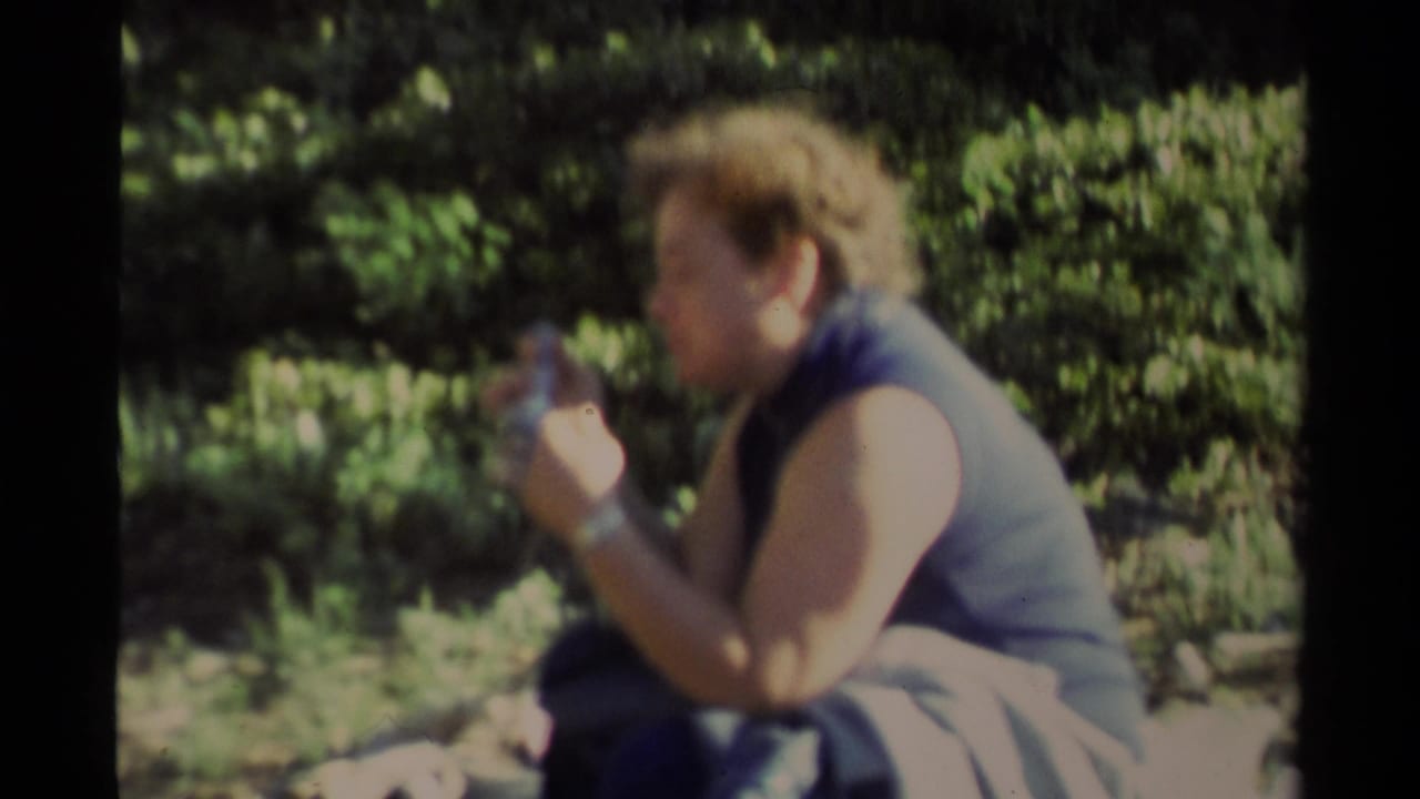 Adult in profile eating while seated outdoors in a sunny wooded area.