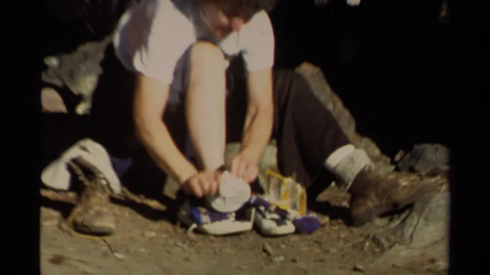 Final Lake Tahoe home-movie frame focuses on a child adjusting shoes, with socks, dirt, rocks, and nearby adult boots visible.