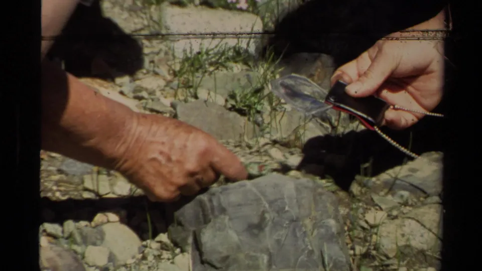 Close 8mm frame from the Lake Tahoe camping scene showing hands near rocky ground and a small object being handled.